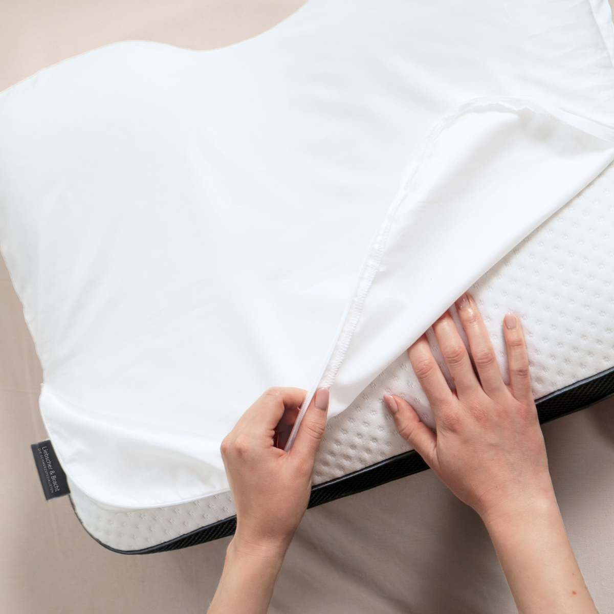 Die Hände sind beim Abnehmen oder Anpassen eines weißen Liebscher & Bracht 2er-Pack: Baumwoll-Kissenbezug auf einem konturierten Memory Foam-Kissen mit strukturierter Oberfläche.