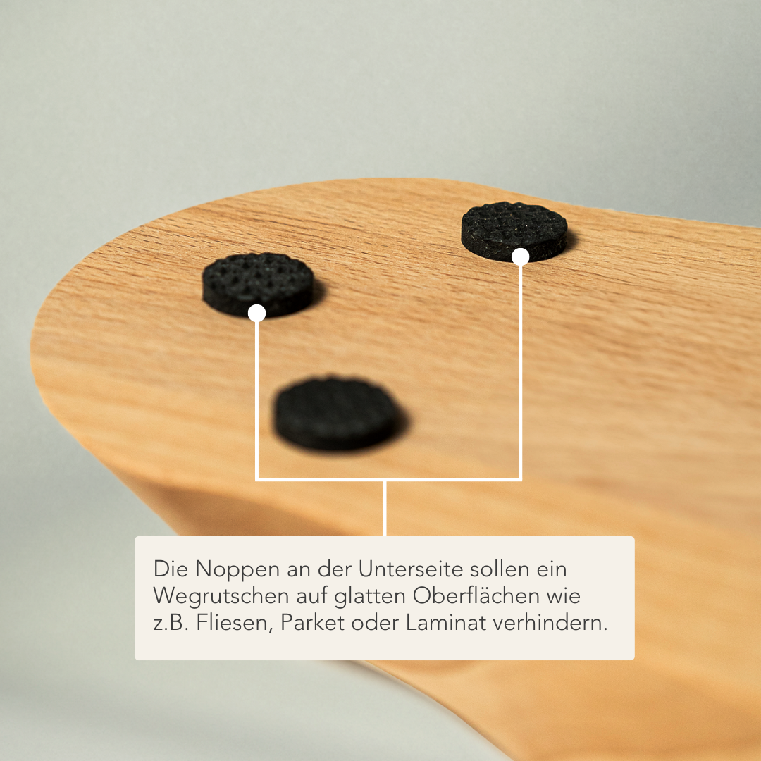 Drei runde schwarze Gummipads werden an der Unterseite einer Holzoberfläche angebracht, um ein Ausrutschen auf glatten Böden wie Fliesen, Parkett oder Laminat zu verhindern. Ein Etikett in deutscher Sprache erklärt diese Funktion.