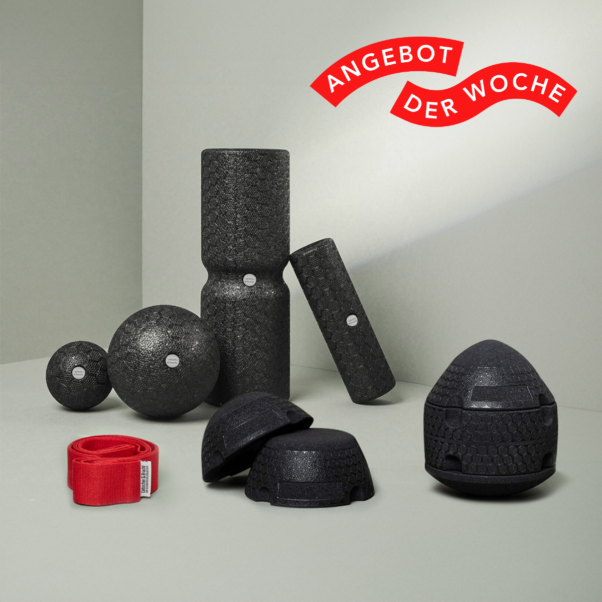 Das Dein ISG-Ischias-Paket von Liebscher & Bracht: Schwarze strukturierte Schaumstoffrollen, Massagebälle und rotes Trainingsband auf grauem Hintergrund. Rotes Label oben rechts: ANGEBOT DER WOCHE - ideal für individuelles Training.