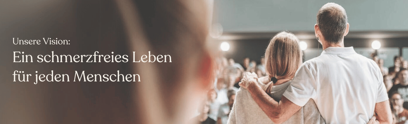 Ein Mann und eine Frau stehen nebeneinander, mit Blick auf ein Publikum, wobei der Mann den Arm um die Frau legt. Der Text auf Deutsch lautet: Unsere Vision: Ein schmerzfreies Leben für jeden Menschen.