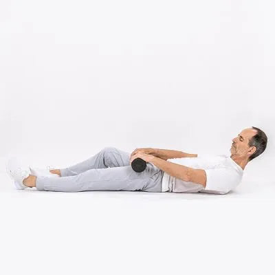 Ein Mann in einem weißen Hemd und einer grauen Hose liegt auf dem Rücken auf dem Boden und hält eine Hantel auf seinem Bauch, die Knie sind leicht gebeugt.