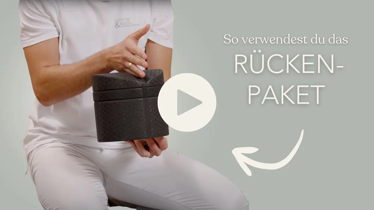 Eine Person in weißer Kleidung hält mit einer Hand eine schwarze, strukturierte Schachtel und gestikuliert mit der anderen. Der deutsche Text lautet: So verwendest du das RÜCKEN-PAKET. Außerdem sind eine Play-Taste und ein Pfeil zu sehen.