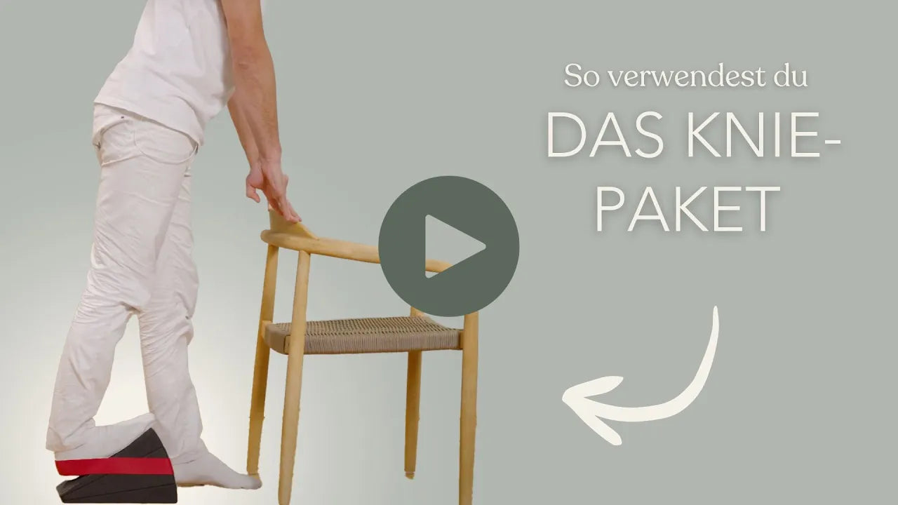 Eine Person in weißer Kleidung steht auf einem schwarz-roten Schaumstoffkeil und hält sich an der Lehne eines Holzstuhls fest. Der deutsche Text lautet: So verwendest du DAS KNIE-PAKET" mit einem weißen Pfeil, der nach rechts zeigt.