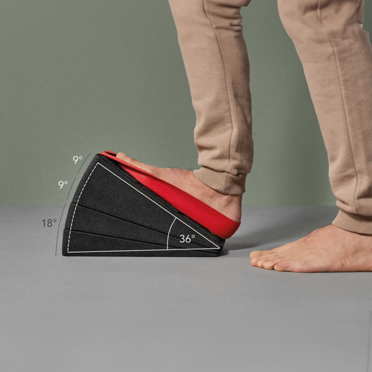 Jemand streckt seinen Fuß auf dem Liebscher & Bracht Dein Knie-Paket aus schwarzem Schaumstoff mit verstellbaren Winkeln (9°, 18°, 27°, 36°) und Trittschlaufe, in beiger Hose auf grauem Boden.