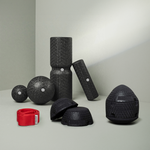 Auf einer grauen Fläche ist ein Satz schwarzer Strukturschaumrollen, Bälle und Kuppeln aus dem Dein ISG-Ischias-Paket von Liebscher & Bracht angeordnet, daneben eine rote Übungs-Schlaufe vor hellgrauem Hintergrund.