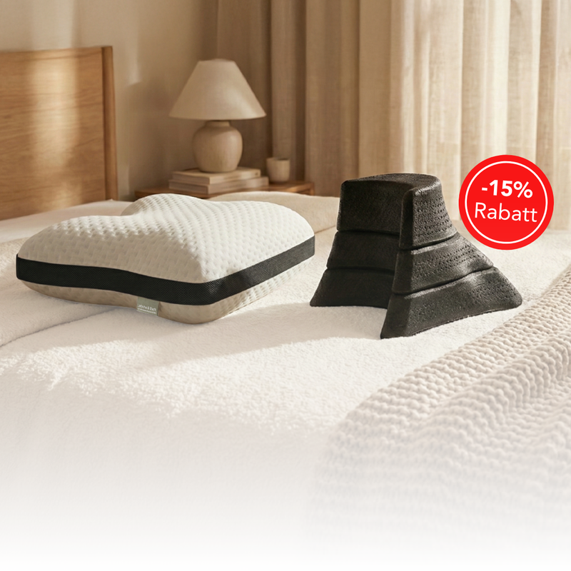 Herzförmiges weißes Kissen und ein Stapel schwarzer Schaumstoff-Keilkissen auf einem ordentlich gemachten Bett in einem gemütlichen Schlafzimmer. Ein roter Kreis weist auf einen Rabatt von 15 % hin (Rabatt).