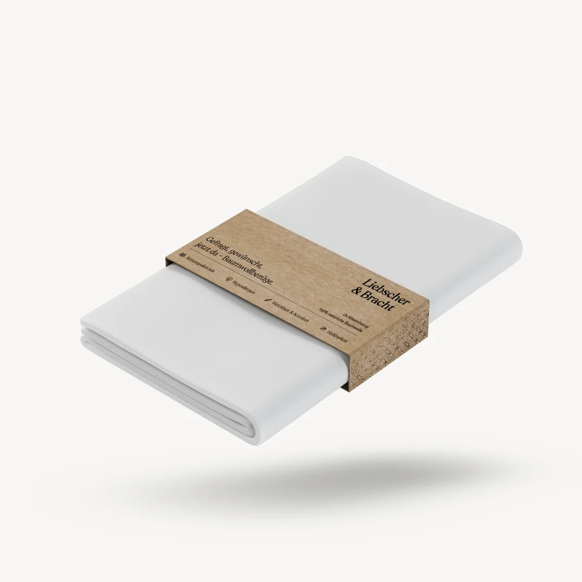 Zwei ordentlich gefaltete „Viereckiger Kissenbezug“-Kissenbezüge (2er-Pack) von Liebscher & Bracht, umwickelt mit einem braunen Papierband, auf dem das Markenlogo und Produktdetails zu sehen sind, vor einem schlichten weißen Hintergrund.