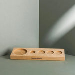 Das Aufbewahrungsbrett von Liebscher & Bracht ist ein rechteckiges Holztablett mit fünf runden, abgestuften Vertiefungen zur Aufnahme eines Drücker-Sets, das auf einer grauen Fläche mit passendem Hintergrund steht und den Markennamen trägt.