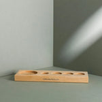 Ein Liebscher & Bracht Aufbewahrungsbrett mit fünf unterschiedlich großen kreisrunden Vertiefungen hält ein Drücker-Set auf einer grauen Fläche und Wand, der Markenname ist auf der Vorderseite aufgedruckt, während weiches Licht sanfte Schatten wirft.