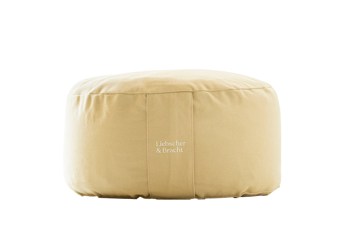Ein runder, beiger Stoff-Pouf aus dem „Übungskissen-Set“ von Liebscher & Bracht mit dem aufgedruckten Markennamen auf der Vorderseite, abgebildet vor einem schlichten weißen Hintergrund.