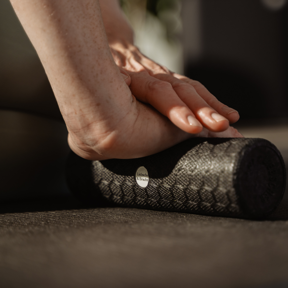 Nahaufnahme einer Person, die das Faszien-Rollmassage-Set von Liebscher & Bracht am Unterarm anwendet, während sie auf einer Matte sitzt – zur Muskelmassage, zur Entspannung oder zur Verbesserung der Beweglichkeit im Rahmen einer Physiotherapie.