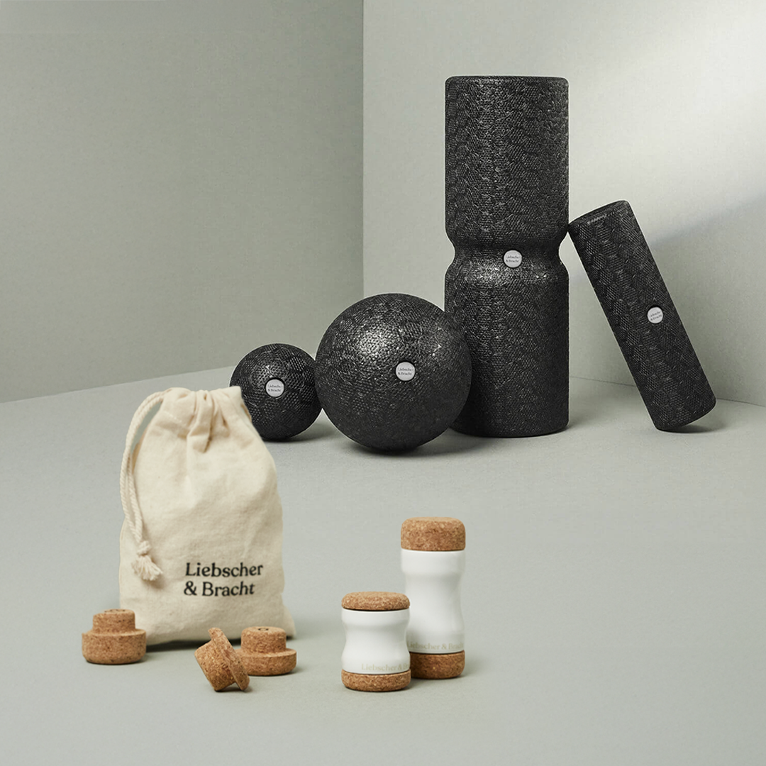 Dein Kiefer-Paket von Liebscher & Bracht besteht aus schwarzen, strukturierten Schaumstoffrollen, Massagebällen, weißen Keramikbehältern mit Korkdeckeln und einer beigen Liebscher & Bracht-Tasche - alles auf hellem Grund für ein effektives Faszien-Training.