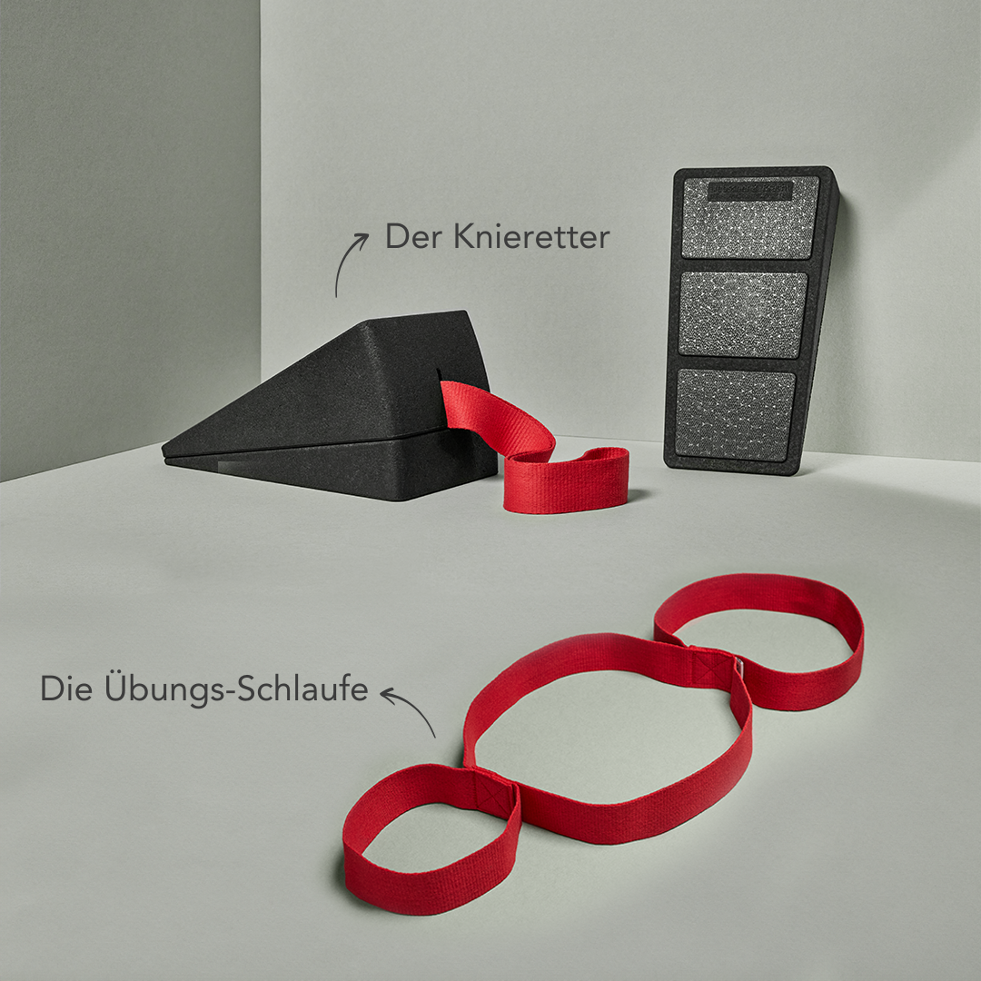Das Liebscher & Bracht Knieretter-Set besteht aus einem schwarzen Knieretter-Kniekeil und einem aufrecht stehenden, rechteckigen Polster, vor dem eine rote Übungs-Schlaufe mit drei Schlaufen flach liegt.