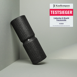 Eine schwarze MAXI-Faszienrolle mit Wirbelsäulen-Entlastung von Liebscher & Bracht für große Körperflächen lehnt an einer hellgrünen Wand. Oben rechts steht: Kaufkompass Testsieger: Liebscher & Bracht Faszienrolle 11/2024.