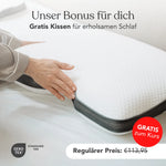 Nahaufnahme einer Person, die ein weißes Kissen mit schwarzem Rand auf ein Bett legt. Deutscher Text wirbt für ein kostenloses Kissen (113,95 €) mit dem Kurs "Gesunder Schlaf - Energie durch Erholung" von Liebscher & Bracht, "GRATIS zum Kurs" im roten Kreis.