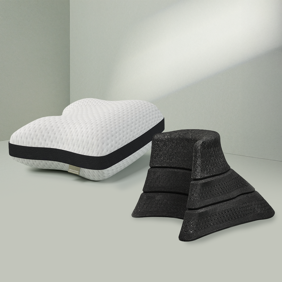 Das Liebscher & Bracht Kissen + Nackenretter Set besteht aus einem weißen, konturierten Kissen mit einem schwarzen Band und vier schwarzen, strukturierten Schaumstoffkeilen, die auf einer hellgrünen Fläche vor einer passenden Wand angeordnet sind.