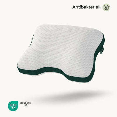 Ein konturiertes weißes Liebscher & Bracht Kissen Clean+ mit strukturierter Oberfläche und dunkelgrünen Rändern schwebt auf einem hellen Hintergrund. Text-Highlights "Antibakteriell" und "OEKO TEX STANDARD 100" neben einem antibakteriellen Symbol, ideal für verschiedene Schlafpositionen.