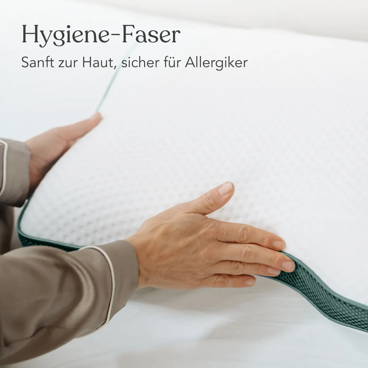 Eine Person im Schlafanzug hält das weiße Liebscher & Bracht Kissen Clean+ mit einem grünen Rand. Der Text auf Deutsch lautet: Hygiene-Faser. Sanft zur Haut, sicher für Allergiker - ideal für verschiedene Schlafpositionen.
