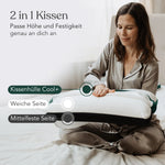 Eine Frau im Pyjama sitzt auf einem Bett und verstellt ein Liebscher & Bracht Kissen Clean+. Das Bild zeigt den Cool+-Bezug und die beiden Komfortseiten für alle Schlafpositionen, während ein deutscher Text die Verstellbarkeit des Kissens erklärt.