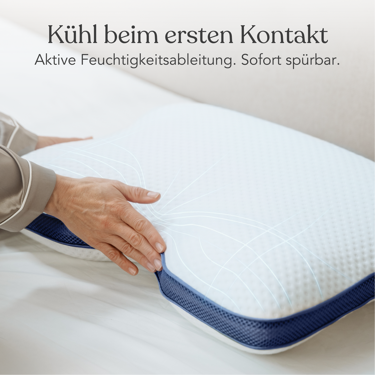 Eine Hand berührt die Liebscher & Bracht Cool+ Kissenhülle, einen weißen Kopfkissenbezug mit blauem Rand auf einem Bett. Der deutsche Text darüber lautet: Kühl beim ersten Kontakt. Aktive Feuchtigkeitsableitung. Sofort spürbar.