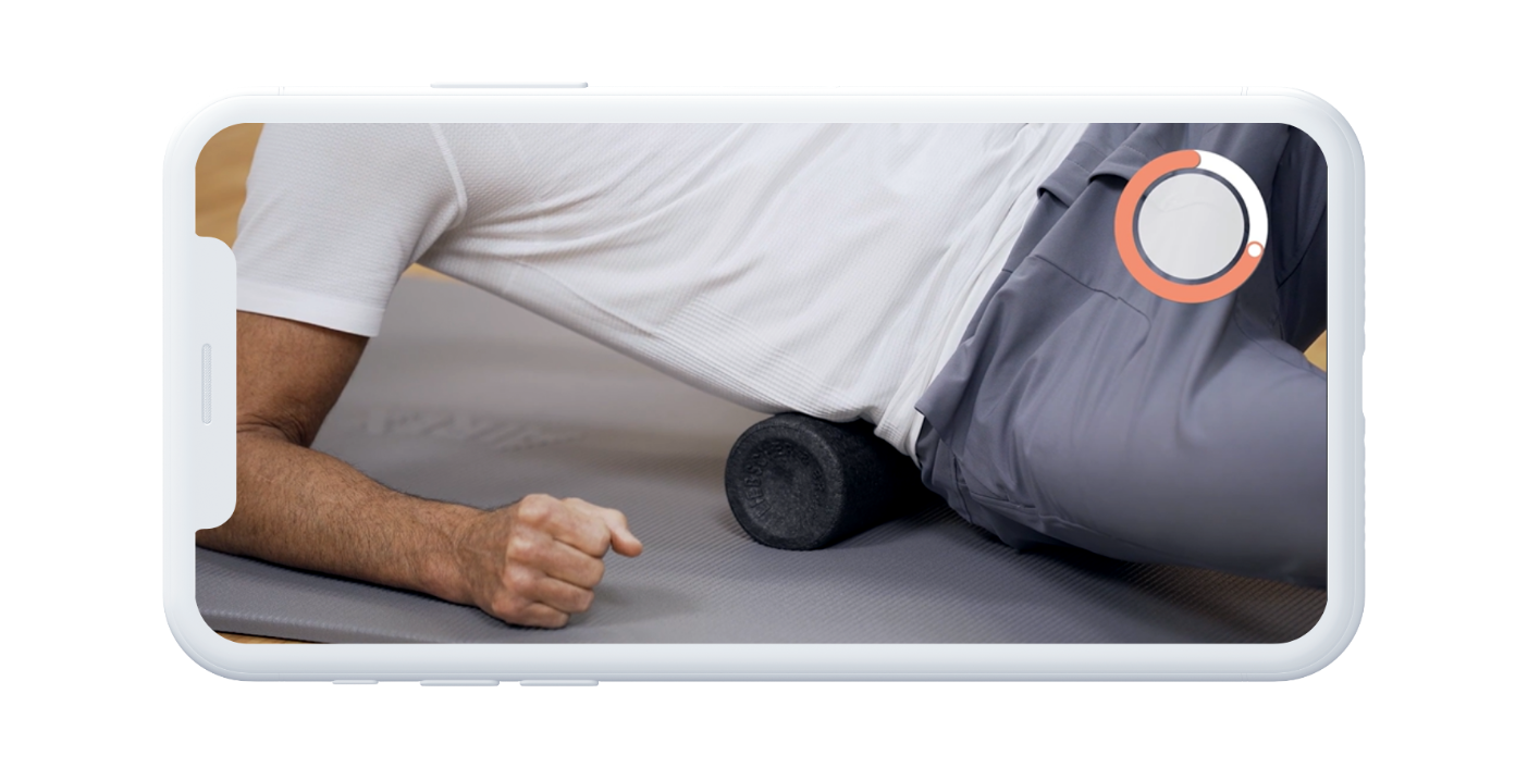 Eine Person in einem weißen Hemd und einer grauen Hose benutzt eine schwarze Schaumstoffrolle an der Hüfte, während sie auf einer Yogamatte liegt, zu sehen durch den Bildschirm eines weißen Smartphones.