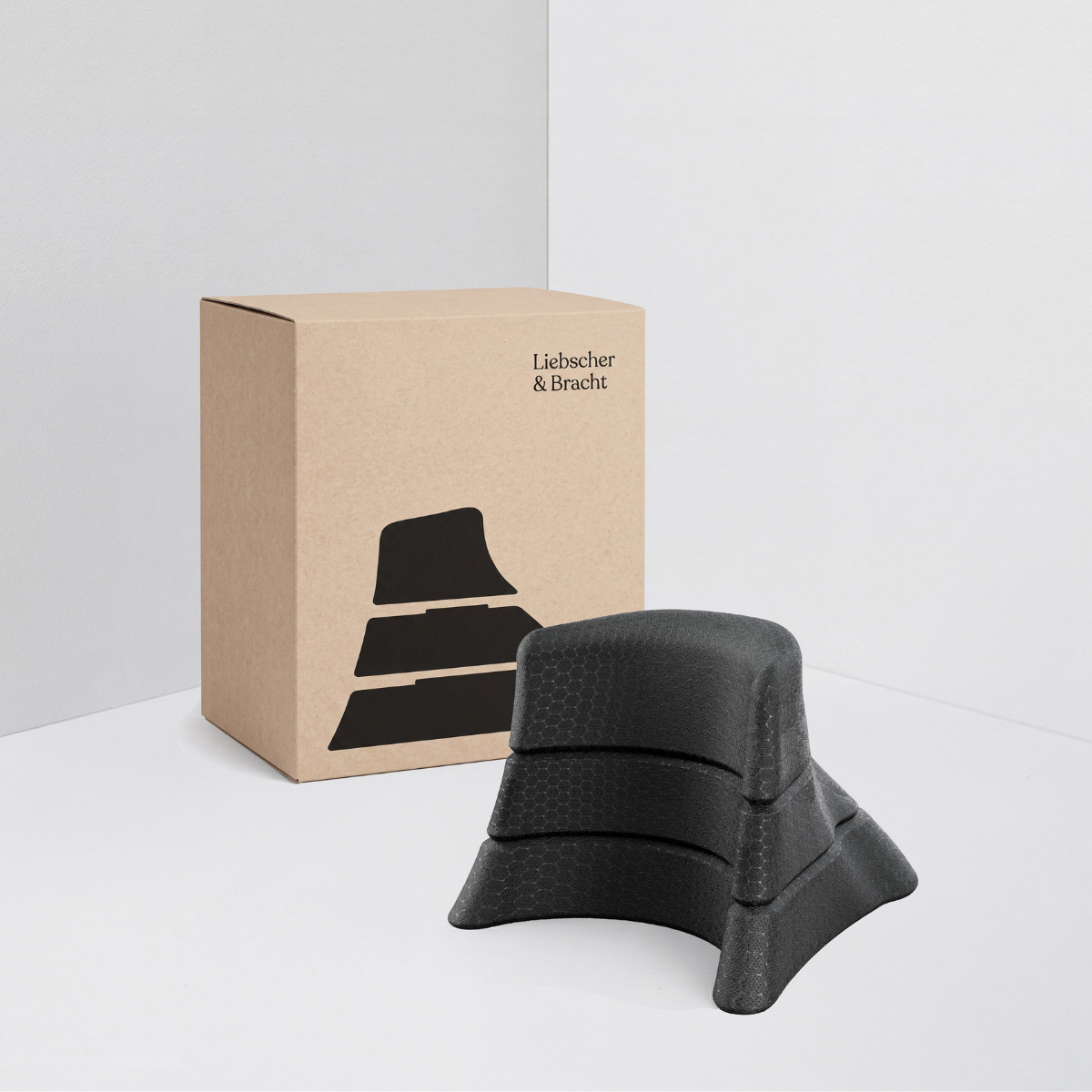 „Der Nackenretter“ von Liebscher & Bracht – ein stapelbarer schwarzer Stützblock aus Schaumstoff – ist vor einer braunen Markenverpackung mit seiner Silhouette abgebildet, ideal für Übungen gegen Nackenschmerzen. Der schlichte weiße Hintergrund hebt das Produkt hervor.