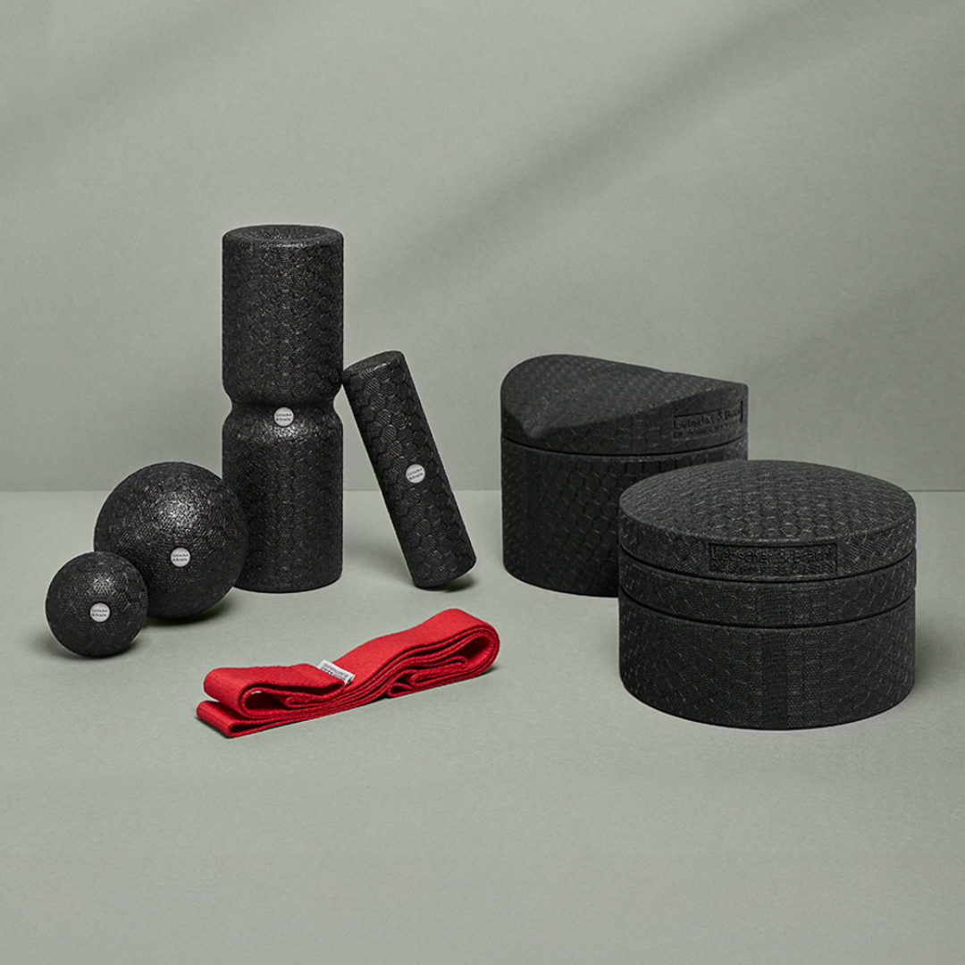 Das Liebscher & Bracht Dein Rücken-Paket enthält schwarz strukturierte Faszienrollen, Massagebälle, Blöcke und ein rotes Gymnastikband auf hellgrünem Untergrund - ideal für die Selbstmassage als umfassendes Faszien-Set.