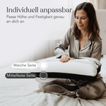 Eine Frau im Pyjama sitzt im Schneidersitz auf einem Bett und verstellt ein Liebscher & Bracht Kissen + Kissenbezüge Set. Der deutsche Text hebt die individuell anpassbare Konstruktion des Kissens mit weichen und mittelfesten Seiten hervor, die eine ruhige und gemütliche Umgebung schaffen.