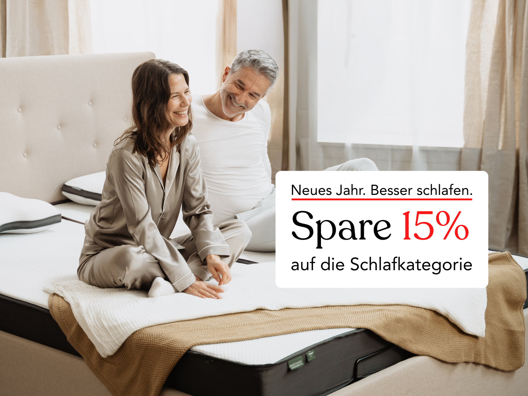 Ein lächelndes Paar in Pyjamas sitzt auf einem Bett in einem hellen Schlafzimmer. Der eingeblendete Text in deutscher Sprache bietet einen Rabatt von 15 % auf schlafbezogene Produkte für das neue Jahr.