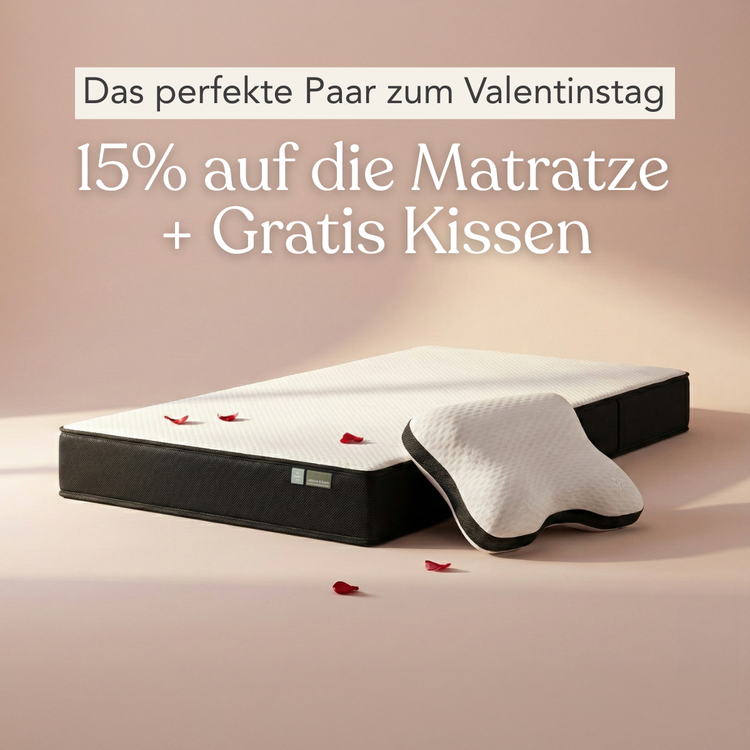 Eine Matratze mit einem Kissen darauf und verstreuten Rosenblättern. Der Text auf Deutsch lautet: "Das perfekte Paar zum Valentinstag. 15% auf die Matratze + Gratis Kissen.