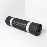 Eine schwarze, rutschfeste Rolands-Übungsmatte von Liebscher & Bracht mit weißem Logo ist aufgerollt und liegt in einer hellen Ecke.