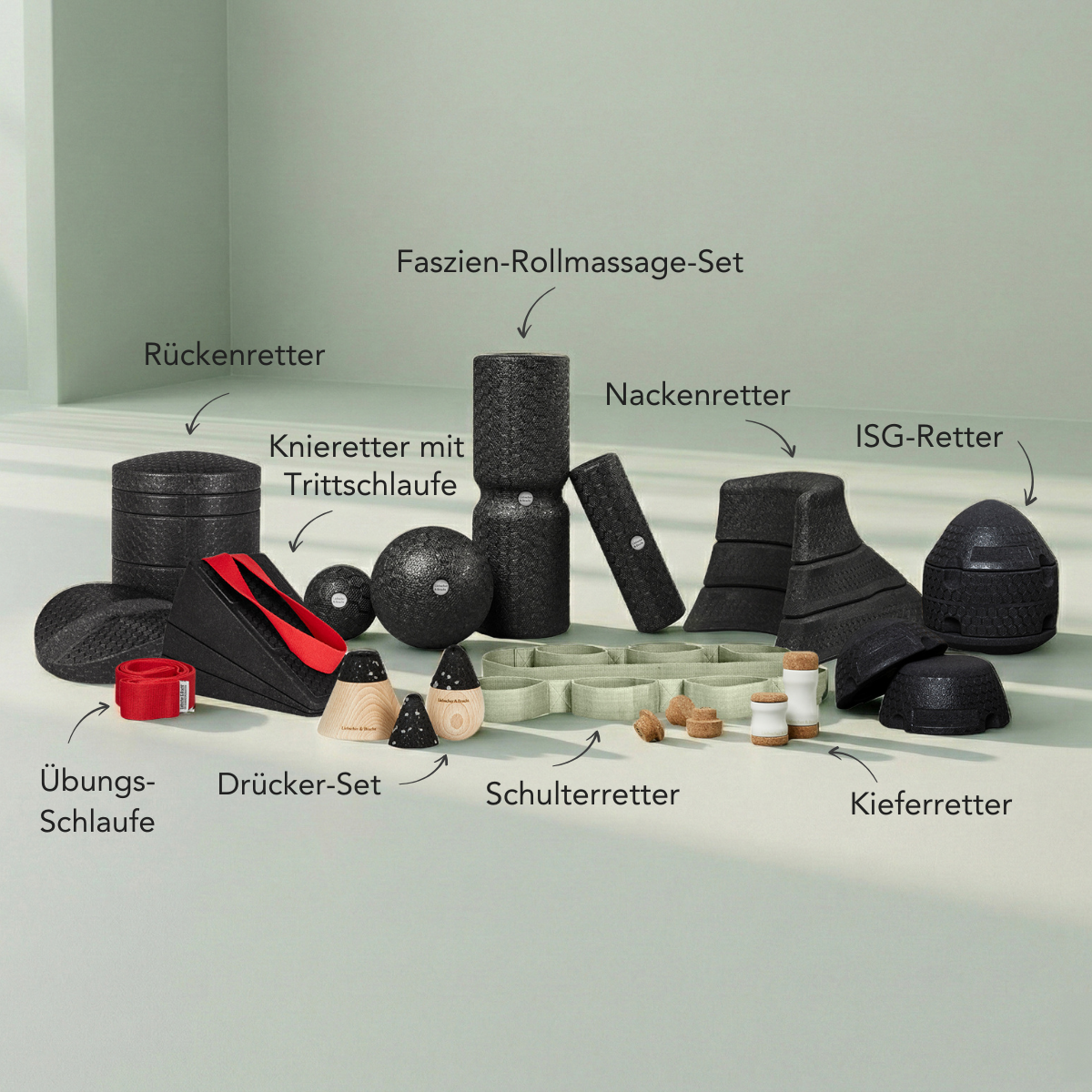 Auf einer hellen Fläche ist eine Auswahl schwarzer Schaumstoff-Massage- und Trainingsgeräte aus dem Dein Komplett-Paket von Liebscher & Bracht ausgestellt, die jeweils in deutscher Sprache beschriftet sind, darunter Rollen, Bälle, Bänder und verschieden geformte Auflagen.
