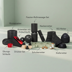 Auf einer hellen Fläche ist eine Auswahl schwarzer Schaumstoff-Massage- und Trainingsgeräte aus dem Dein Komplett-Paket von Liebscher & Bracht ausgestellt, die jeweils in deutscher Sprache beschriftet sind, darunter Rollen, Bälle, Bänder und verschieden geformte Auflagen.