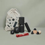 Das Angebots-Paket von Liebscher & Bracht mit schwarzen, texturierten Foam Rollern, Bällen, Kegeln, roter Übungsschlaufe und beigem Beutel mit Muster liegt auf hellgrauem Untergrund vor grauem Hintergrund.