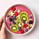 Eine Hand hält eine Schale mit rosa Smoothie mit Kiwi, Beeren, Müsli und Mandelblättchen - ein köstliches Beispiel für gesunde Ernährung mit Abnehmen garantiert von Liebscher & Bracht.