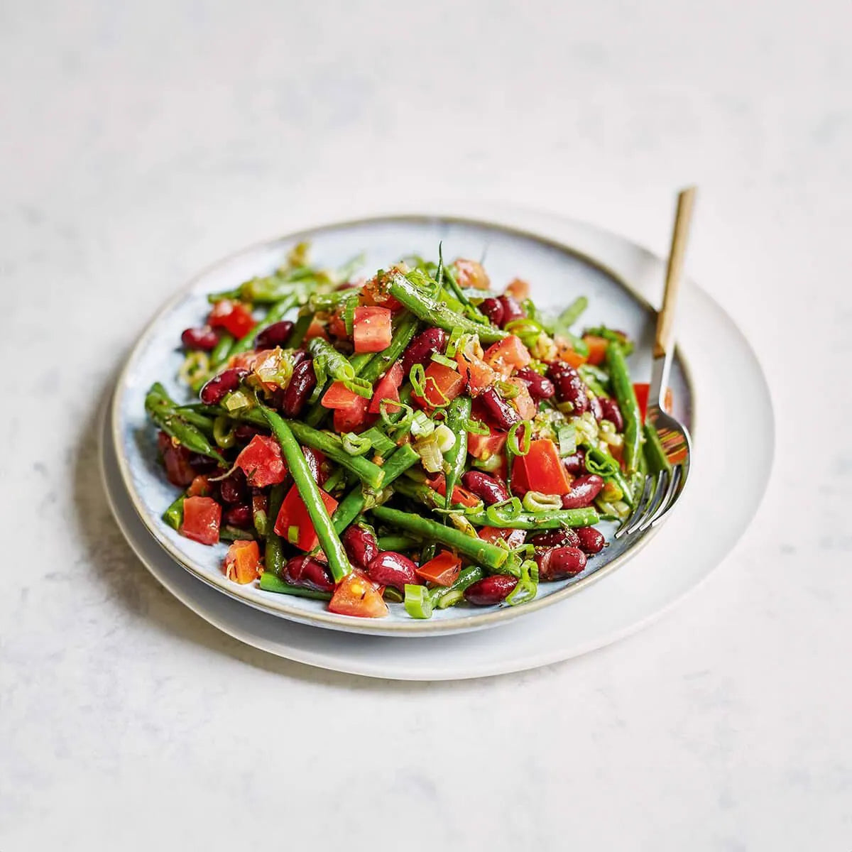 Ein lebendiger Bohnensalat mit grünen Bohnen, Kidneybohnen, Tomaten und grünen Zwiebeln - ideal für vegane Rezepte aus dem Intervallfasten Kochbuch von Liebscher & Bracht.