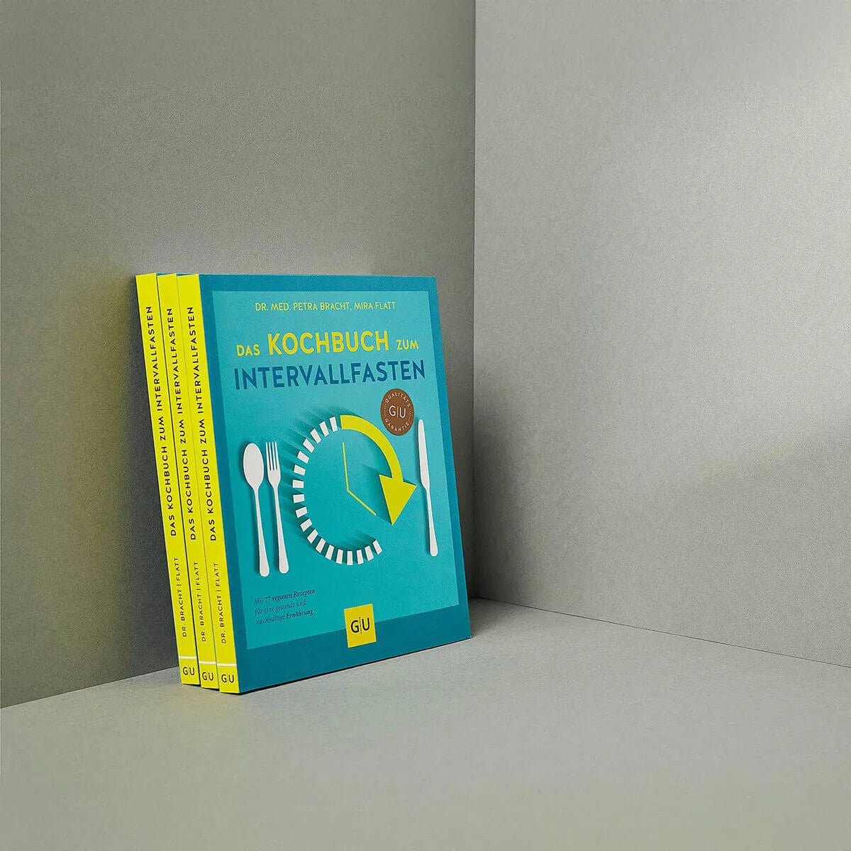 Vier Exemplare des Intervallfasten Kochbuchs von Liebscher & Bracht sind so gestapelt, dass ein Cover nach vorne zeigt und drei Buchrücken vor einem schlichten grauen Hintergrund zu sehen sind - ideal, um vegane Rezepte zu entdecken.