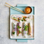 Ein weißes Tablett mit fünf frischen Gemüse-Frühlingsrollen, Dip-Sauce und Essstäbchen auf blauem Hintergrund - ideal für Rezepte aus dem Intervallfasten Kochbuch von Liebscher & Bracht.