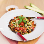 Ein Teller mit Zucchininudeln, Kirschtomaten, Basilikum und Croutons ist ein Beispiel für gesunde Ernährung - ideal für die Verwendung von Intervallfasten von Liebscher & Bracht. Gabel und Messer liegen auf dem Teller, im Hintergrund sind Zucchinischeiben und Croutons zu sehen.