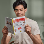 Ein dunkelhaariger Mann in einem hellen Hemd sitzt im Haus und liest das Buch "Kieferschmerzen & Zähneknirschen selbst behandeln" von Liebscher & Bracht, das ein wirksames Übungsprogramm gegen Kieferschmerzen und Zähneknirschen bietet.