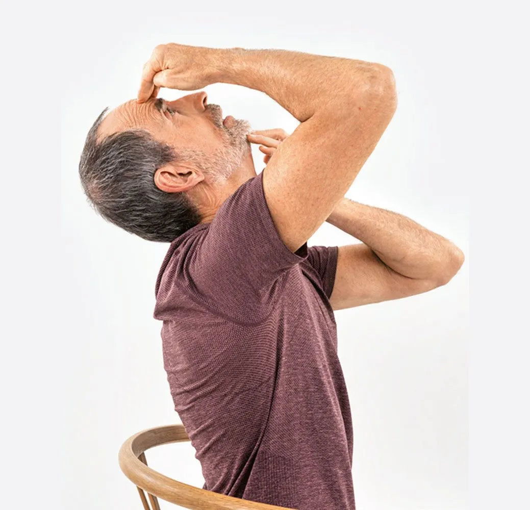 Ein Mann, der auf einem Stuhl sitzt, neigt den Kopf zurück, schließt ein Nasenloch und macht eine Atemübung - möglicherweise nach dem Programm "Kieferschmerzen & Zähneknirschen selbst behandeln" von Liebscher & Bracht.