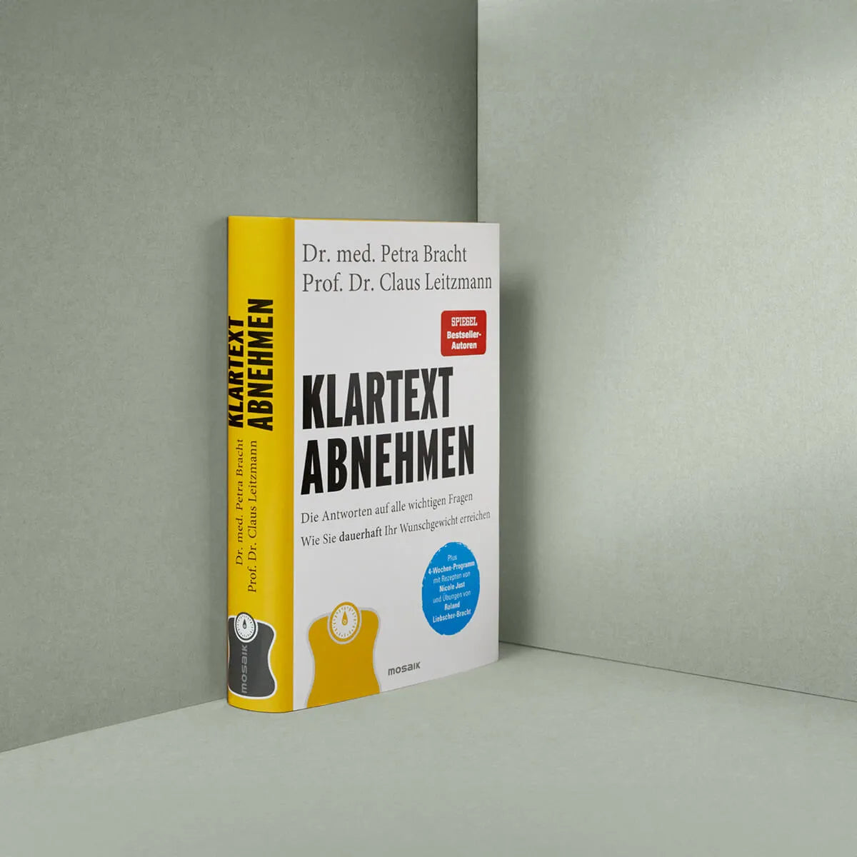 Das Hardcover-Buch "Klartext Abnehmen" von Liebscher & Bracht steht aufrecht auf einer hellgrauen Fläche vor einer grauen Wand und zeigt auf seinem weiß-gelben Einband mit schwarz-roter Schrift ein 4-Wochen-Programm zum Erreichen des Idealgewichts.