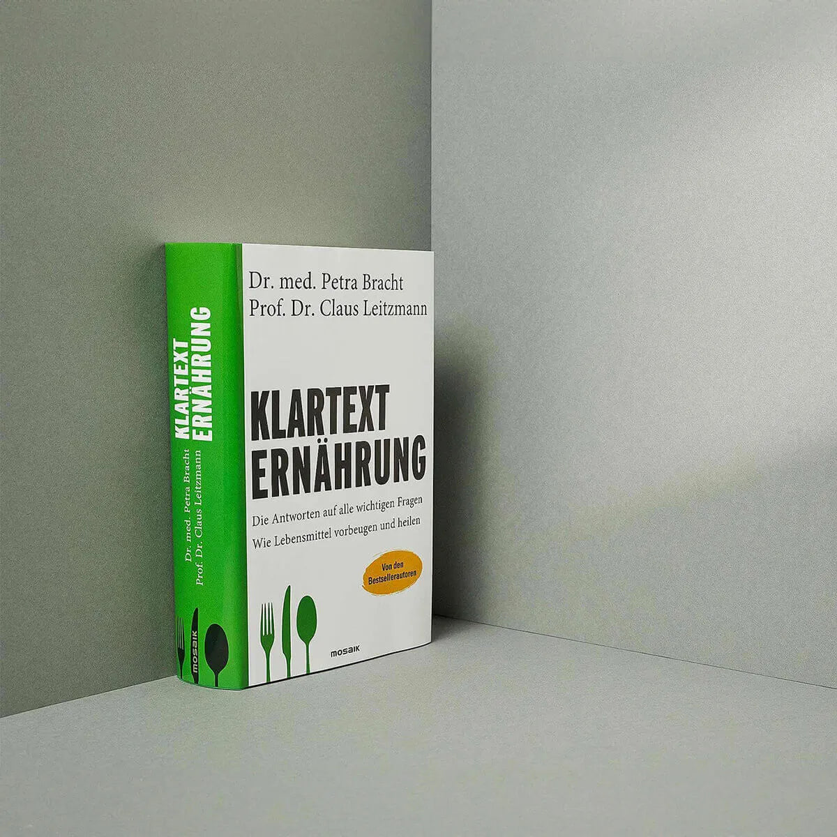 Das deutsche Buch "Klartext Ernährung: Die Antworten auf alle wichtigen Fragen" von Liebscher & Bracht steht aufrecht vor einem grauen Hintergrund und zeigt ein grün-weißes Cover mit Gabel-, Messer- und Löffelsymbolen.