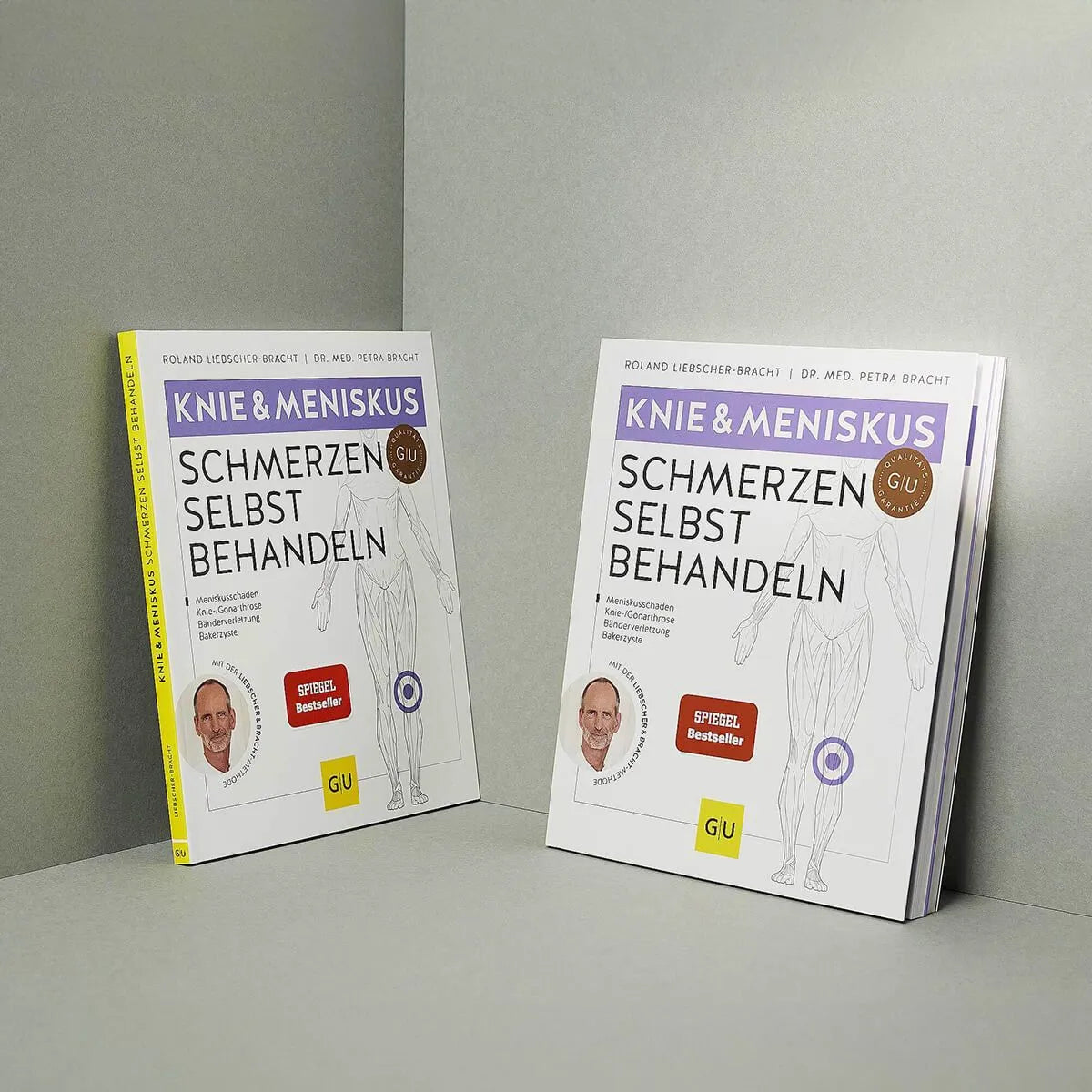 Zwei Exemplare von Knieschmerzen selbst behandeln von Liebscher & Bracht stehen auf einer grauen Fläche. Das Cover zeigt ein Knieschmerzen-Relief, ein Übungs-Programm, medizinische Illustrationen, Autorenfotos und ein rotes Bestseller-Label.
