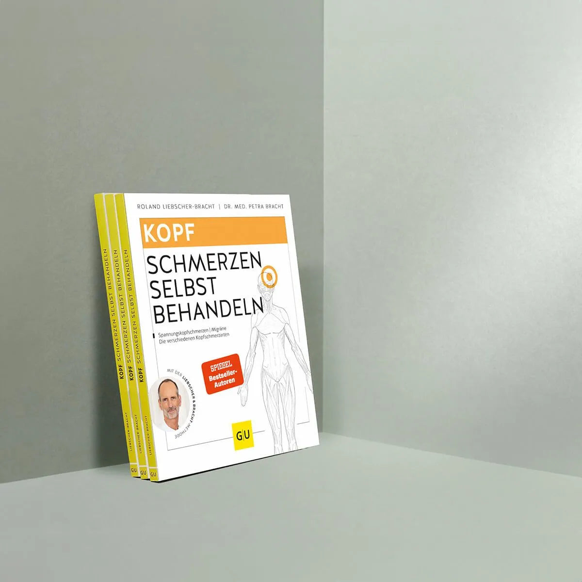 Drei Exemplare von "Kopfschmerzen selbst behandeln" von Liebscher & Bracht stehen aufrecht auf einer minimalistischen, hellgrauen Fläche, die eine Strichzeichnung von Kopf und Schulter zeigt - perfekt für alle, die Kopfschmerzen lindern wollen.