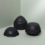 Drei schwarze Der ISG-Ischias-Retter von Liebscher & Bracht, ideal zur Verbesserung der Beweglichkeit im Hüft- oder Gesäßbereich, stehen in Dreiecksformation auf einer hellgrauen Fläche vor einem passenden Hintergrund.