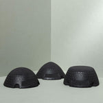 Drei schwarz strukturierte, kuppelförmige Liebscher & Bracht Der ISG-Ischias-Retter-Objekte ruhen auf einer hellgrauen Fläche in einer hellgrauen Ecke, jeweils in unterschiedlichen Winkeln angeordnet. Eingerückte rechteckige Abschnitte deuten ihre Beweglichkeits-Trainingsfunktion an.