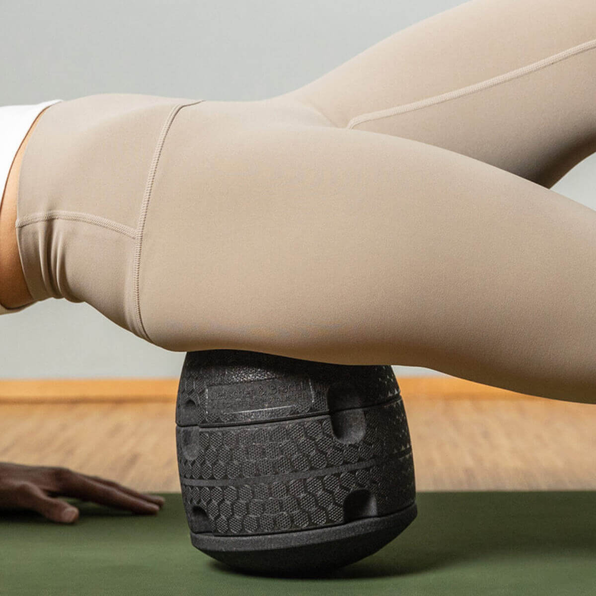 Eine Person liegt auf der Seite und benutzt den strukturierten schwarzen Der ISG-Ischias-Retter von Liebscher & Bracht unter der Hüfte auf einer grünen Übungsmatte, um die Beweglichkeit zu verbessern.