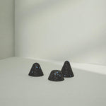 Drei kleine, dunkle, strukturierte Drücker-Aufsätze Hart von Liebscher & Bracht, jeweils mit winzigen blauen Sprenkeln, sind auf einer glatten hellgrauen Oberfläche angeordnet - ideal für gezielte Druck-Stimulation bei Verspannungen.