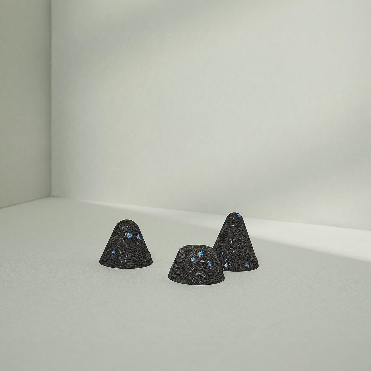 Drei kleine, dunkle, strukturierte Drücker-Aufsätze Hart von Liebscher & Bracht, jeweils mit winzigen blauen Sprenkeln, sind auf einer glatten hellgrauen Oberfläche angeordnet - ideal für gezielte Druck-Stimulation bei Verspannungen.